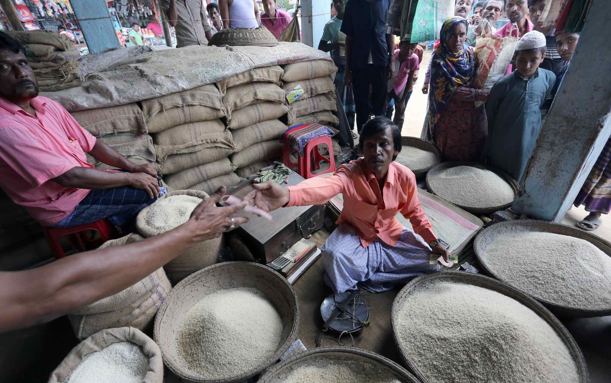 Rice vendor seated, surrounded by containers of rice, handing money to an outstretched hand